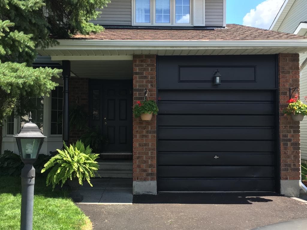 Home entrance with a freshly painted black front door and garage door framed by red brick